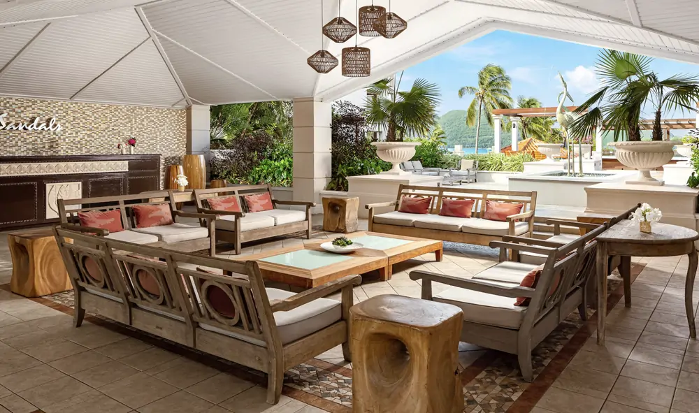 Open-air lounge with wicker seating and a view toward the pool at Sandals Grande St. Lucian