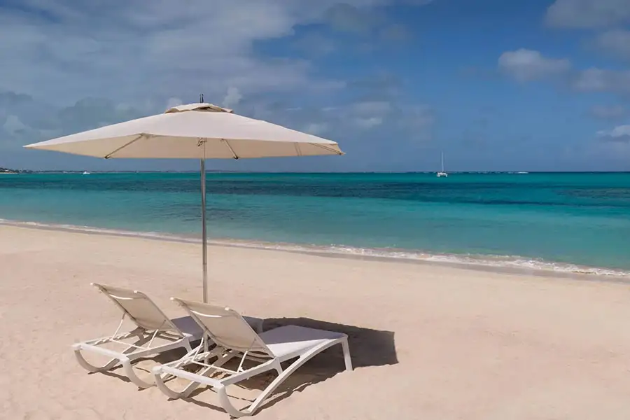 Beach loungers under an umbrella by turquoise water at Beaches Exuma