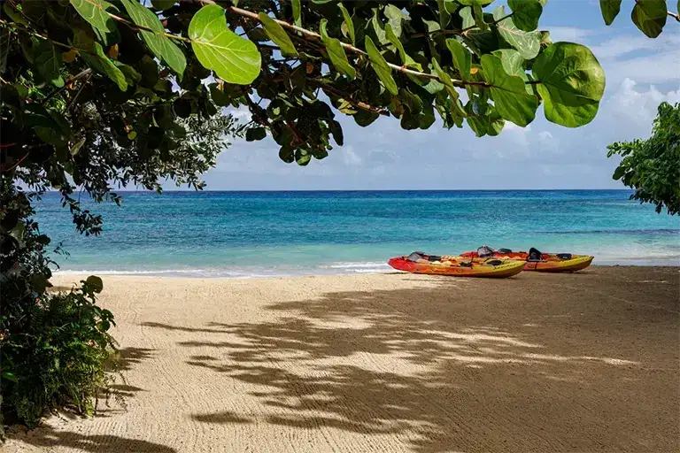 Kayaks resting on the beach under shaded trees at Sandals Ochi Rios