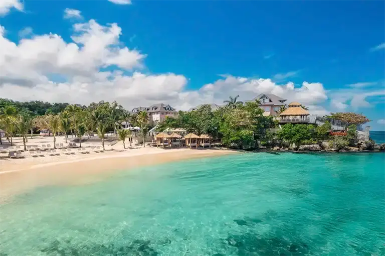 Beach and turquoise water with hillside resort buildings at Sandals Ochi Beach Resort
