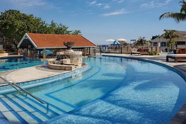 Resort pool with stone fountain feature and thatched-roof structure at Sandals Ochi Rios