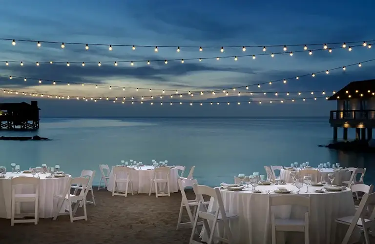 Beachfront dinner setup with string lights at dusk at Sandals Royal Bahamian
