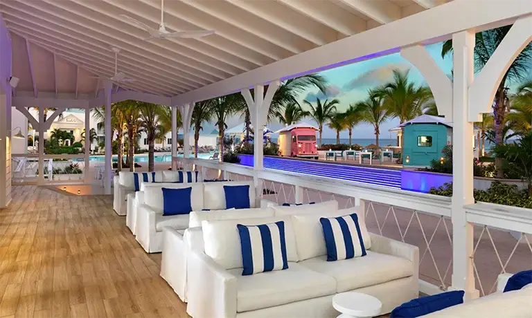 Covered lounge patio with white sofas overlooking the beach at Sandals Royal Bahamian