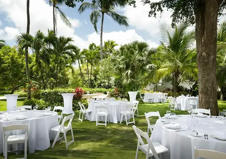Outdoor garden event setup with round tables under palm trees at Sandals Royal Bahamian