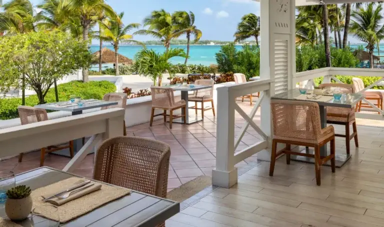 Outdoor dining patio with wicker chairs overlooking the beach at Sandals Royal Bahamian