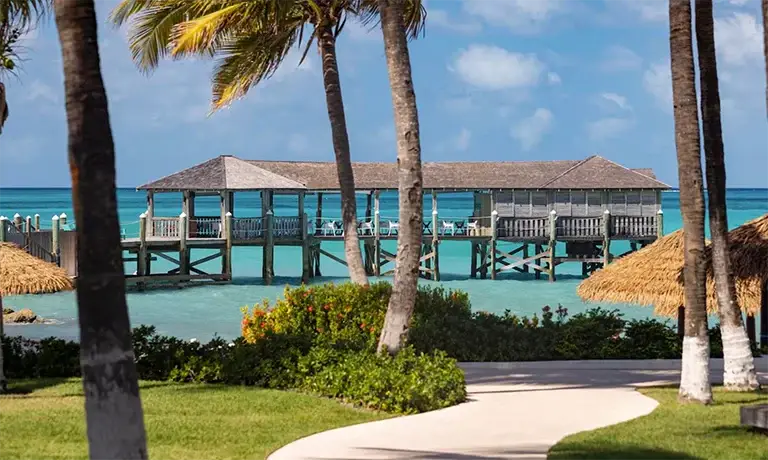 Overwater thatched-roof pier pavilion surrounded by palm trees at Sandals Royal Bahamian