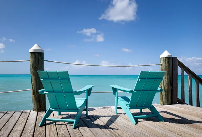Two teal Adirondack chairs on a pier overlooking the ocean at Sandals Royal Bahamian