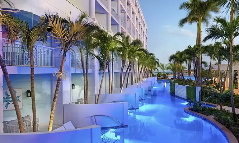 Illuminated pool walkway lined with palm trees at dusk at Sandals Royal Bahamian
