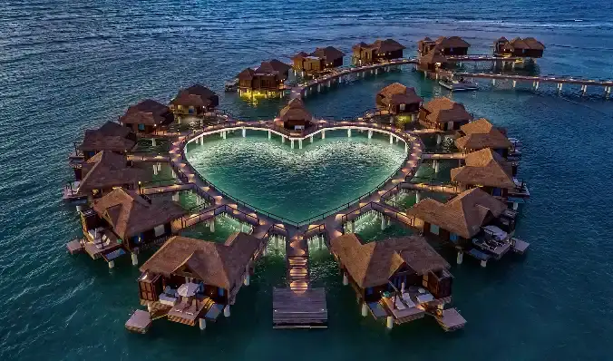 Aerial evening view of the heart-shaped private island of overwater villas at Sandals Royal Caribbean