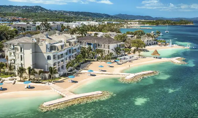 Aerial view of Sandals Royal Caribbean resort with hillside greenery and beach