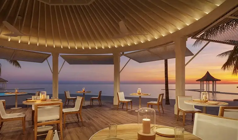 Open-air overwater restaurant at Sandals Royal Caribbean with candlelit tables and ocean sunset view