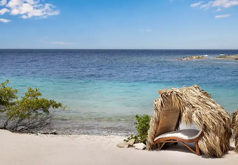 Thatched-roof beach lounge chair overlooking the ocean at Sandals Royal Curacao
