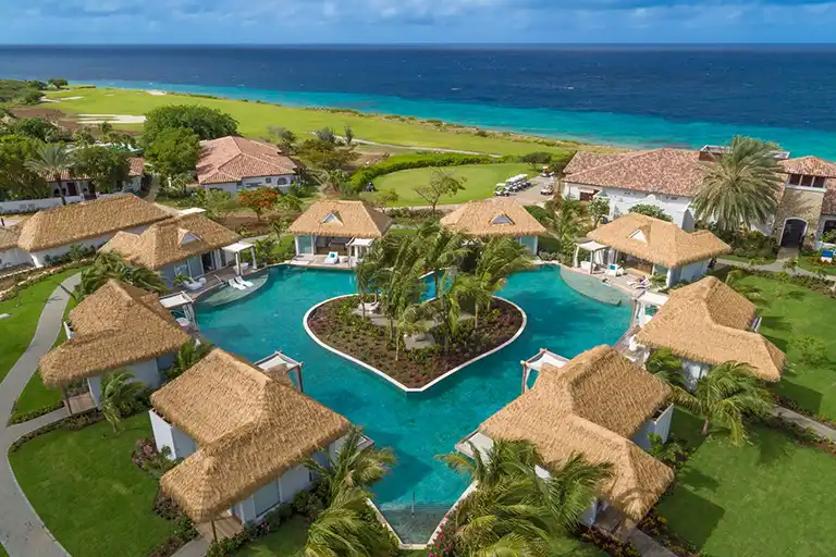 Aerial view of the heart-shaped pool complex surrounded by thatched-roof bungalows at Sandals Royal Curacao
