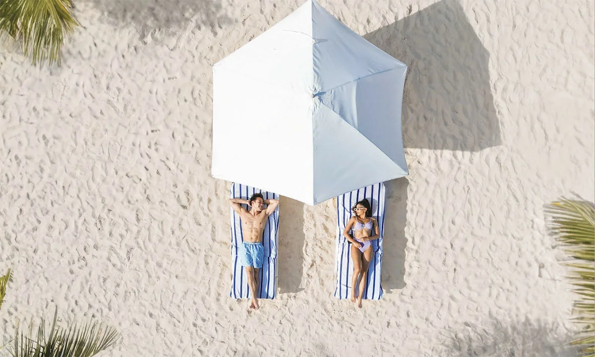 Aerial view of a couple relaxing on lounge chairs under a beach umbrella at Sandals South Coast