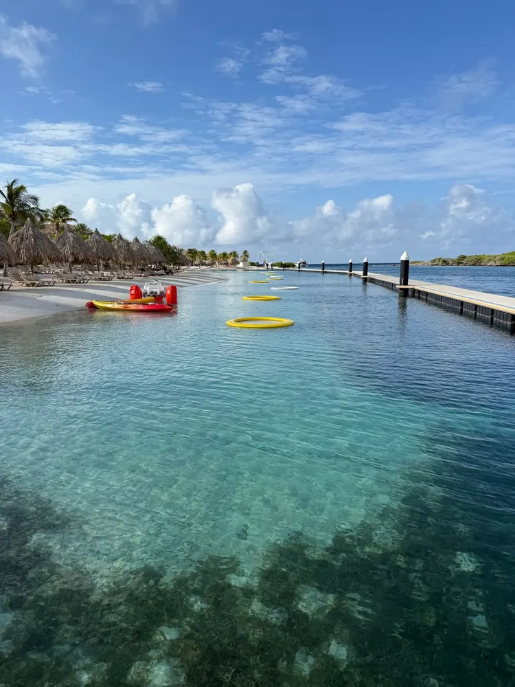 Calm, clear swim area at the Sandals Curaçao beach with yellow floating rafts and the floating bridge