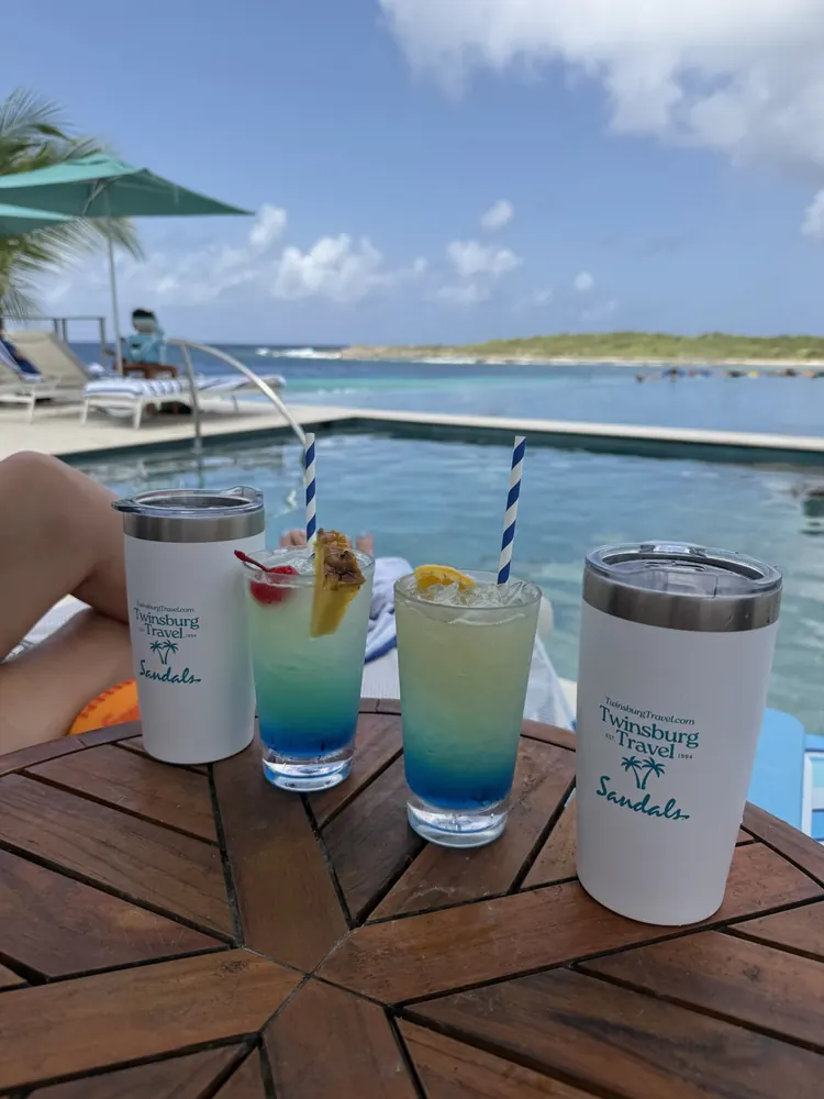 Blue tropical cocktails and Sandals tumblers on a poolside table at Sandals Curaçao